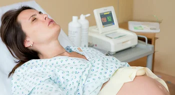 Une femme enceinte allongée sur un lit d’hôpital, en plein travail avant une éventuelle épisiotomie.