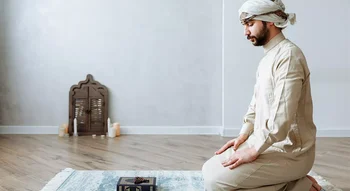 رجل عربي بملابس تقليدية يجلس بخشوع على سجادة صلاة، وأمامه نسخة من القرآن الكريم ومسبحة.