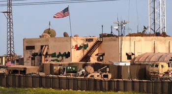 قاعدة عسكرية أمريكية في سوريا تظهر فيها الأعلام والمعدات العسكرية والحواجز الأمنية.