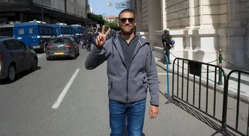 Khaled Drareni affiche un signe de paix devant le tribunal, symbole de sa résilience face à la répression.