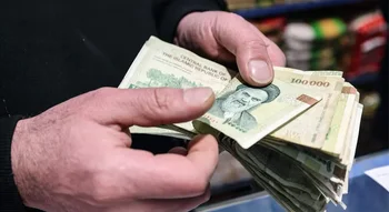 الريال الإيراني (Iranian Rial): شخص يحسب رزمة من الأوراق النقدية من فئة 100 ألف ريال.