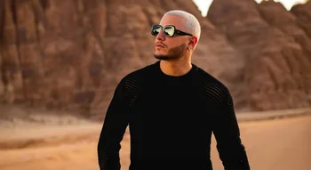 DJ Snake posant fièrement dans le désert avec des montagnes en arrière-plan.