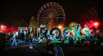 Visiteurs assis autour du célèbre lettrage « Eurocks » illuminé la nuit, symbole des Eurockéennes de Belfort.