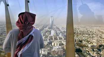 رجل بالزي السعودي ينظر إلى أفق العاصمة الرياض من نافذة برج المملكة.