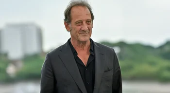 Portrait élégant de Vincent Lindon en veste noire sur fond naturel.