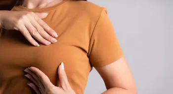 Femme en train de palper sa poitrine à travers un t-shirt, à la recherche d’une éventuelle boule dans le sein.