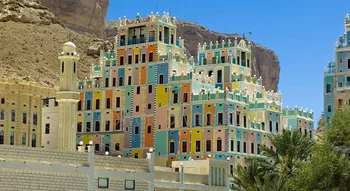 عمارة يمنية (Yemeni Architecture): مباني تاريخية ملونة متعددة الطوابق في حضرموت بجوار جبل صخري ومئذنة مسجد.