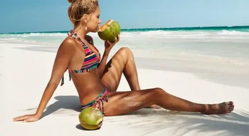 Une femme boit une noix de coco fraîche sur la plage, profitant des bienfaits de l'eau de mer.