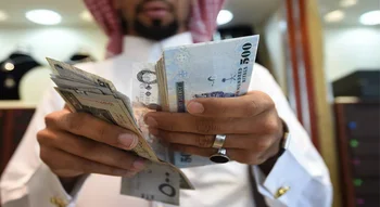 رجل يرتدي الزي العربي التقليدي يحسب أوراقاً نقدية من فئة 500 ريال قطري.