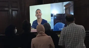 Khaled Drareni apparaît à l’écran pendant une audience, dans un contexte marqué par les répercussions de la guerre d’Algérie.