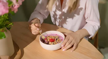 Une femme en chemise blanche mange un bol de smoothie aux fruits et aux graines, un repas sain recommandé pour l’alimentation pendant les règles.