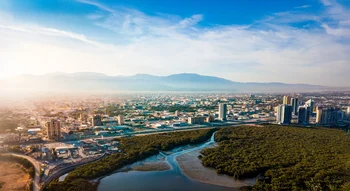 منظر جوي لمدينة ساحلية حديثة تتميز بوجود غابات المانغروف الخضراء وجبال في الأفق.