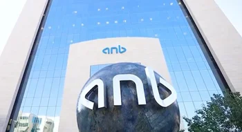 واجهة زجاجية شاهقة لمبنى البنك، يظهر عليها علامة (anb) باللون الأزرق، وأمامها مجسم كروي داكن كبير يحمل نفس العلامة بأحرف بيضاء ثلاثية الأبعاد.