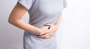 Une femme en robe grise tenant son ventre avec douleur, un symptôme fréquent du kyste de l’ovaire.