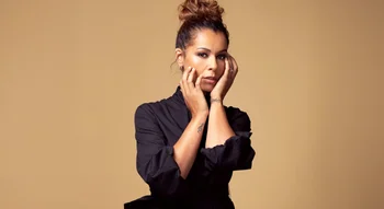 Portrait de Chimène Badi en robe noire, posant les mains sur son visage.