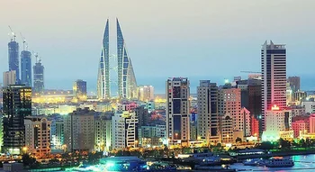 منظر بانورامي لأفق العاصمة المنامة في البحرين وقت الغسق، يبرز فيه مبنى مركز البحرين التجاري العالمي بتصميمه الفريد والأضواء المتلألئة للمدينة.