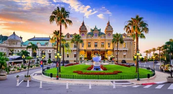 Vue panoramique de la majestueuse façade du Casino de Monte-Carlo, encadrée par des palmiers et baignée d’une lumière dorée en fin de journée.
