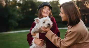 Deux femmes heureuses tenant un chien, représentant l’engagement envers les soins cosmétiques sans cruauté.