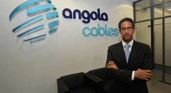 Homme en costume devant le logo de Angola Cables.