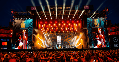 Die Hauptbühne des Jazz Open Stuttgart bei Nacht mit einer beeindruckenden Lichtshow – rote und goldene Scheinwerfer, große LED-Bildschirme mit dem Festival-Logo und Tausende von Zuschauern vor der Bühne