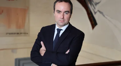 Sébastien Lecornu posant avec les bras croisés dans un bâtiment institutionnel.