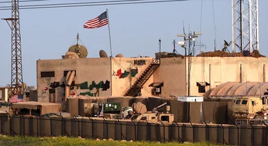 قاعدة عسكرية أمريكية في سوريا تظهر فيها الأعلام والمعدات العسكرية والحواجز الأمنية.