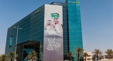 مبنى البنك الأهلي التجاري الزجاجي مزين بلافتة ضخمة تحمل صور القيادة السعودية.
