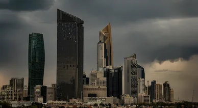 أفق مدينة الكويت مع ناطحات سحاب حديثة مثل برج الحمراء، تطل على المياه تحت سماء داكنة وعاصفة.