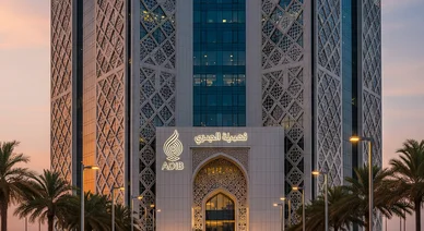 واجهة مبنى مصرف أبوظبي الإسلامي (ADIB) بتصميمه المعماري المزخرف بأنماط هندسية، تبرز علامة المصرف المضيئة فوق المدخل الرئيسي وقت الغروب، وتحيط به أشجار النخيل.