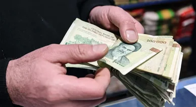 الريال الإيراني (Iranian Rial): شخص يحسب رزمة من الأوراق النقدية من فئة 100 ألف ريال.