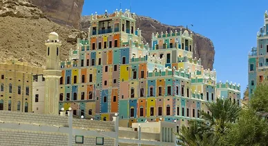 عمارة يمنية (Yemeni Architecture): مباني تاريخية ملونة متعددة الطوابق في حضرموت بجوار جبل صخري ومئذنة مسجد.