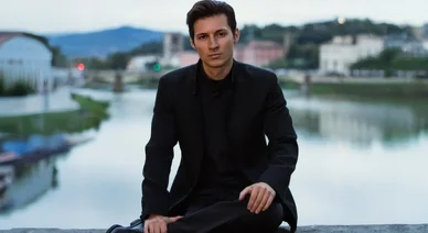 Pavel Dourov assis près d’une rivière, vêtu de noir, regard calme et posé.