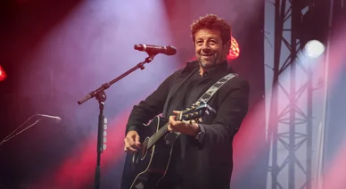 Patrick Bruel jouant de la guitare sur scène pendant un concert.