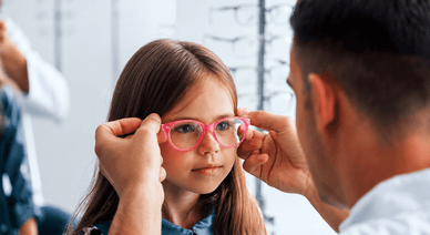 Optiker passt einem Mädchen eine pinke Brille im Fachgeschäft an