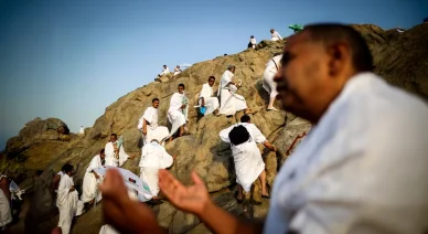 حجاج بملابس الإحرام يتسلقون الصخور في جبل الرحمة بمشعر عرفات ويرفعون أيديهم بالدعاء.