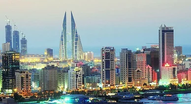 منظر بانورامي لأفق العاصمة المنامة في البحرين وقت الغسق، يبرز فيه مبنى مركز البحرين التجاري العالمي بتصميمه الفريد والأضواء المتلألئة للمدينة.