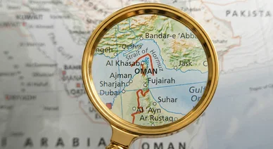 عدسة مكبرة تسلط الضوء على موقع مضيق هرمز الاستراتيجي على خريطة جغرافية.