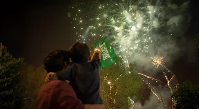 الاحتفال برفع علم السعودية أمام عروض الألعاب النارية المضيئة في سماء الليل.