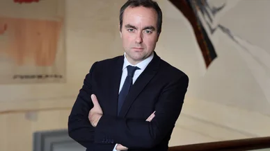 Sébastien Lecornu photographié lors d’une séance officielle. Sébastien Lecornu posant avec les bras croisés dans un bâtiment institutionnel.