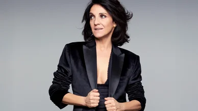 Portrait de studio de Florence Foresti portant une veste de smoking en velours noir sur un fond gris, avec un regard confiant.