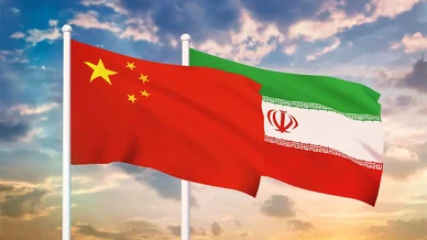 الشراكة الاستراتيجية والتعاون الدبلوماسي بين البلدين أعلام الصين وإيران: علم الصين الأحمر وعلم إيران يرفرفان معاً على ساريتين تحت سماء غائمة وقت الغروب.