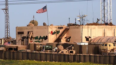 قاعدة عسكرية أمريكية في سوريا تظهر فيها الأعلام والمعدات العسكرية والحواجز الأمنية.