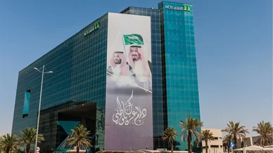 مبنى البنك الأهلي التجاري الزجاجي مزين بلافتة ضخمة تحمل صور القيادة السعودية.