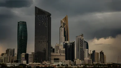 أفق مدينة الكويت مع ناطحات سحاب حديثة مثل برج الحمراء، تطل على المياه تحت سماء داكنة وعاصفة.