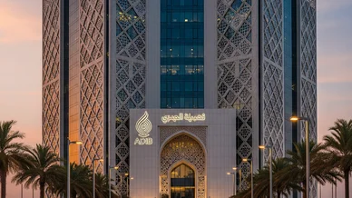 واجهة مبنى مصرف أبوظبي الإسلامي (ADIB) بتصميمه المعماري المزخرف بأنماط هندسية، تبرز علامة المصرف المضيئة فوق المدخل الرئيسي وقت الغروب، وتحيط به أشجار النخيل.