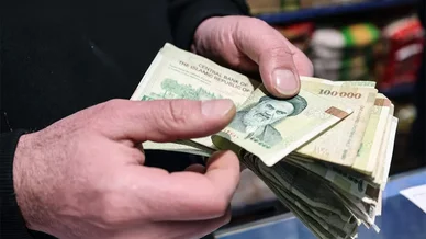 التعاملات المالية اليومية وحركة النقد في الأسواق المحلية الريال الإيراني (Iranian Rial): شخص يحسب رزمة من الأوراق النقدية من فئة 100 ألف ريال.