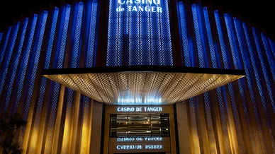 الواجهة المضيئة لكازينو طنجة ليلاً، تتميز بأضواء عمودية زرقاء وتصميم هندسي ذهبي فوق المدخل الرئيسي.