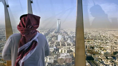 رجل بالزي السعودي ينظر إلى أفق العاصمة الرياض من نافذة برج المملكة.