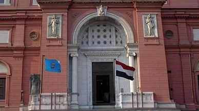 المدخل الرئيسي للمتحف المصري بالقاهرة الواجهة الأمامية للمتحف المصري في القاهرة بلونها الأحمر الوردي المميز، يظهر فيها المدخل الرئيسي ذو القوس الكبير المزين بتماثيل فرعونية، ويرفرف علم جمهورية مصر العربية على يمين السلالم.
