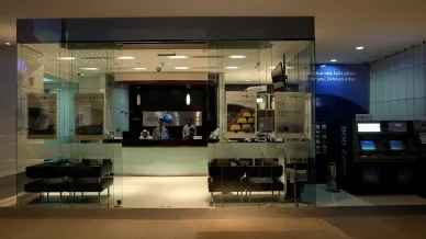 واجهة زجاجية لفرع مصرف أبوظبي الإسلامي (ADIB)، يظهر من خلالها موظفون خلف منصة خدمة العملاء التي تحمل اسم المصرف وعلامته، وتتواجد أجهزة صراف آلي على الجانب الأيمن بجوار لافتة "معكم دائماً على مدار الساعة".